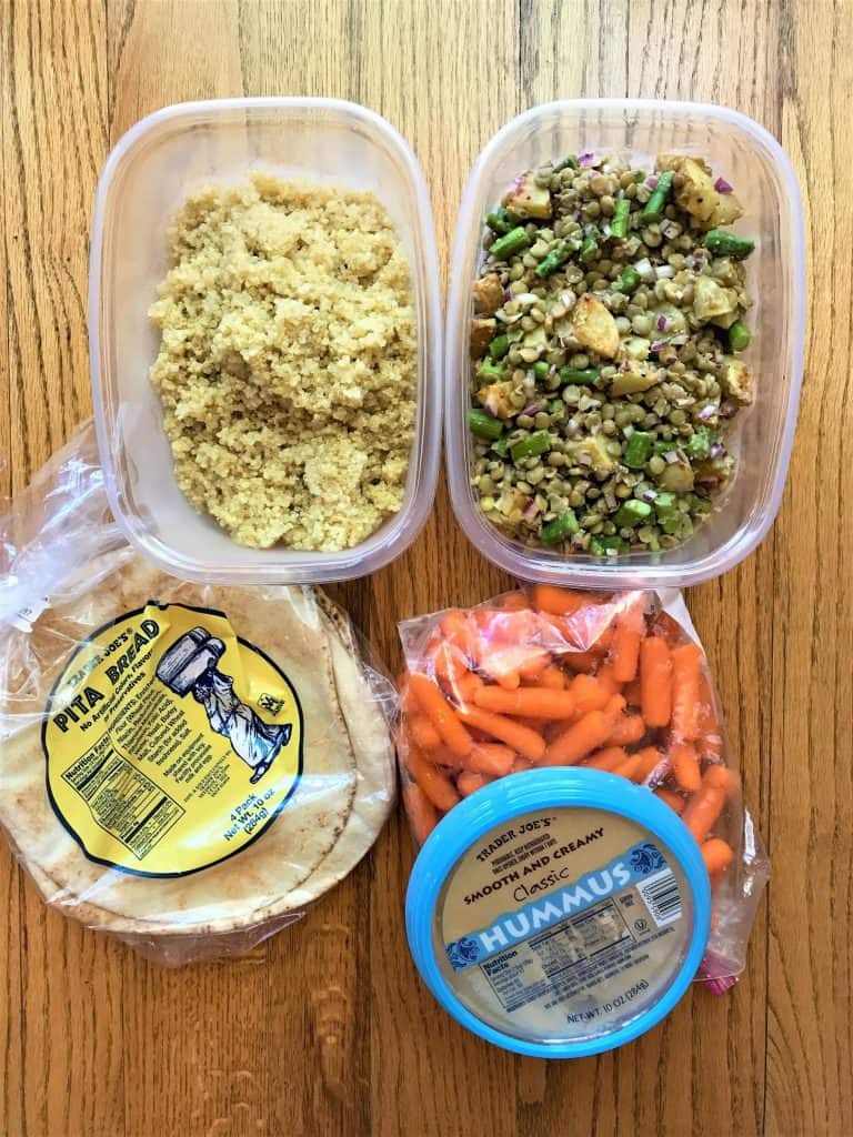 A plastic container filled with different types of food on a table with pita and hummus vegan meal for new mom