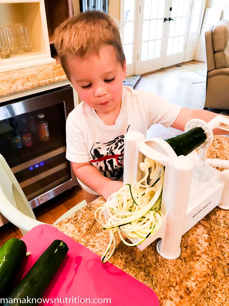 toddler boy standing in kitchen helping to spiralize zucchini