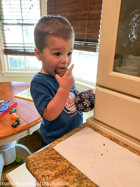 A young boy sitting at a table in front of a window eating cookie bar