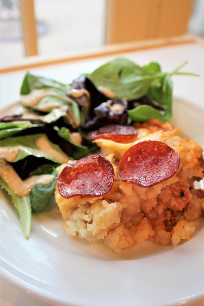 A plate of food on a table, with Pizza and Shepherd\'s pie and salad