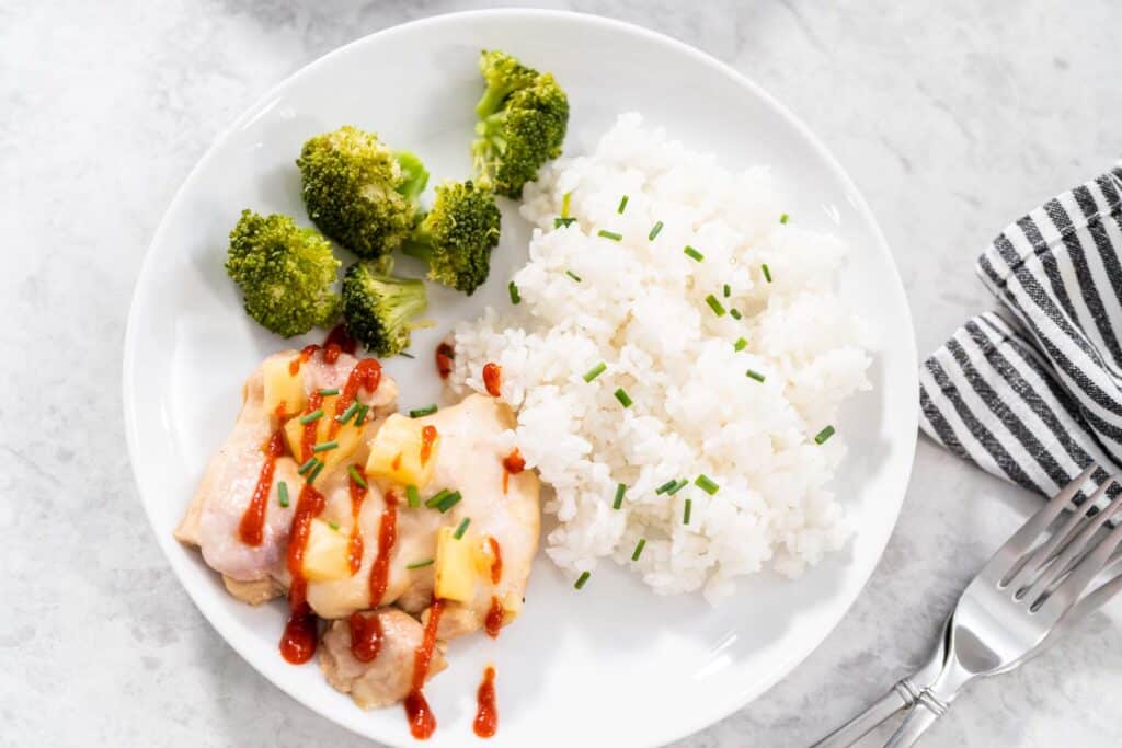 pineapple baked chicken drizzled with sriracha with white rice and broccoli on white plate