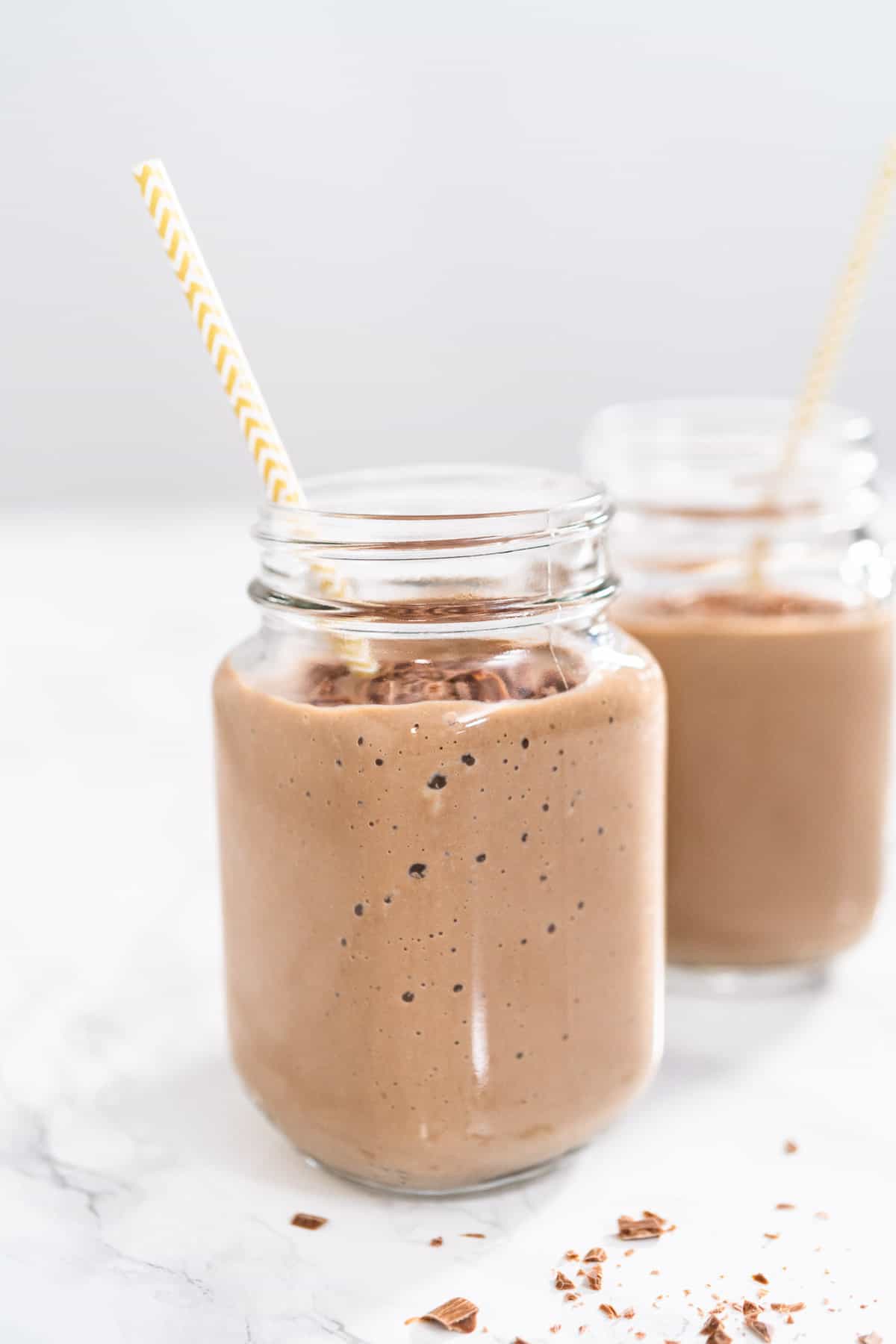 Two healthy chocolate smoothies in glass jars with white background