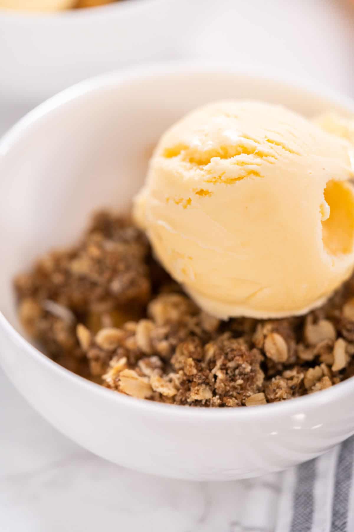 finished apple crisp in a bowl with vanilla ice cream