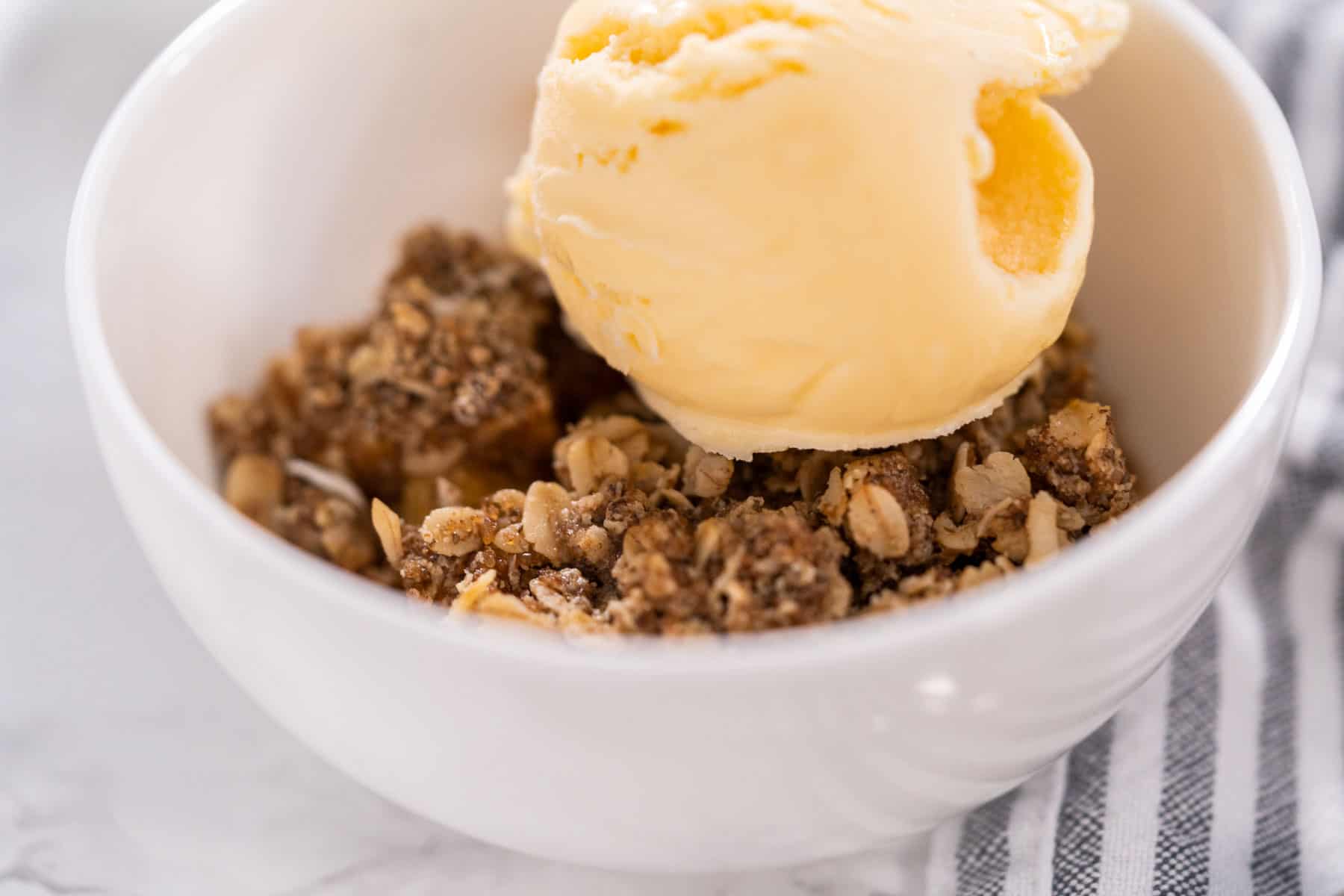 healthy apple crisp with oats and flax and vanilla ice cream on top in a white bowl