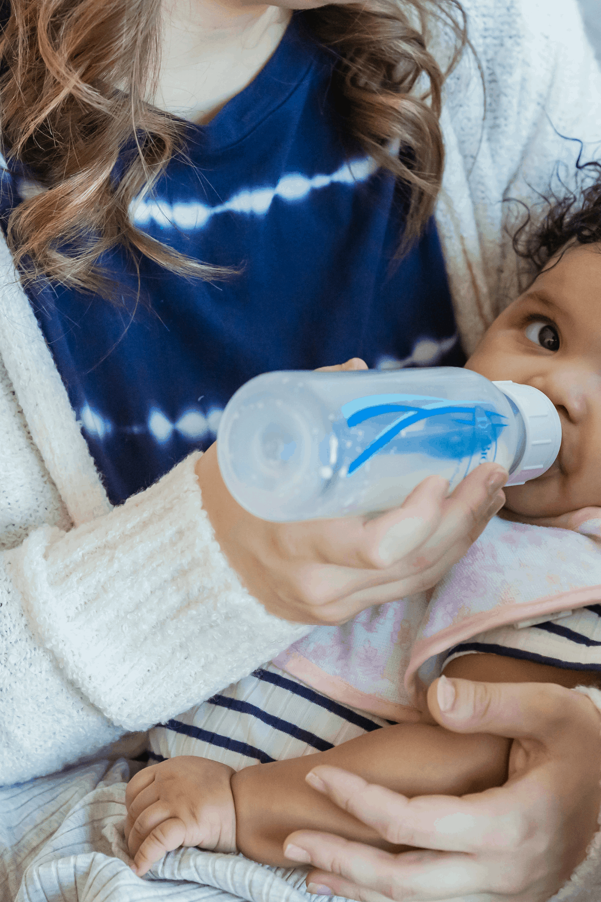 8 month old baby drinking dr browns bottle in mother's arms before offering solids