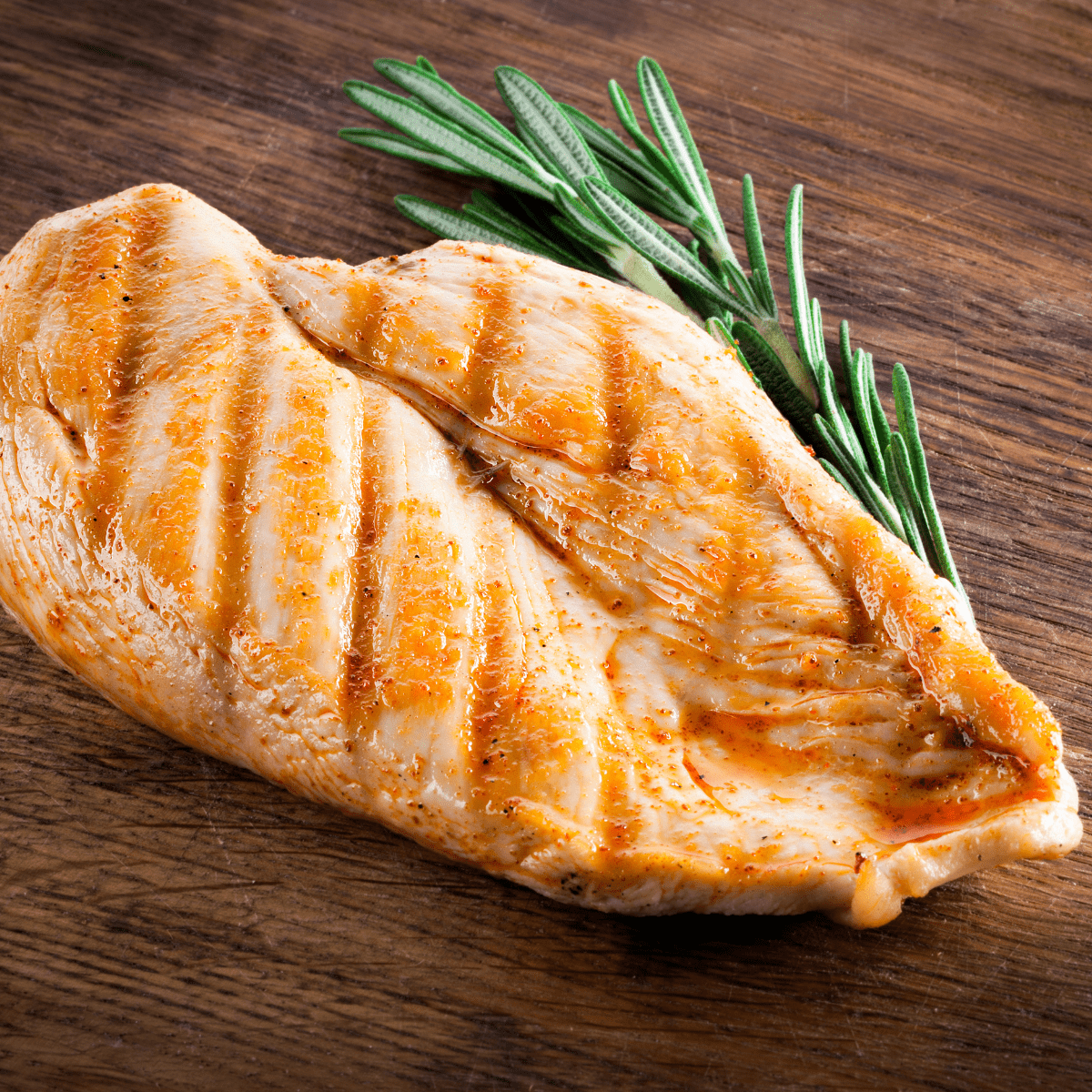 grilled chicken breast on cutting board with rosemary