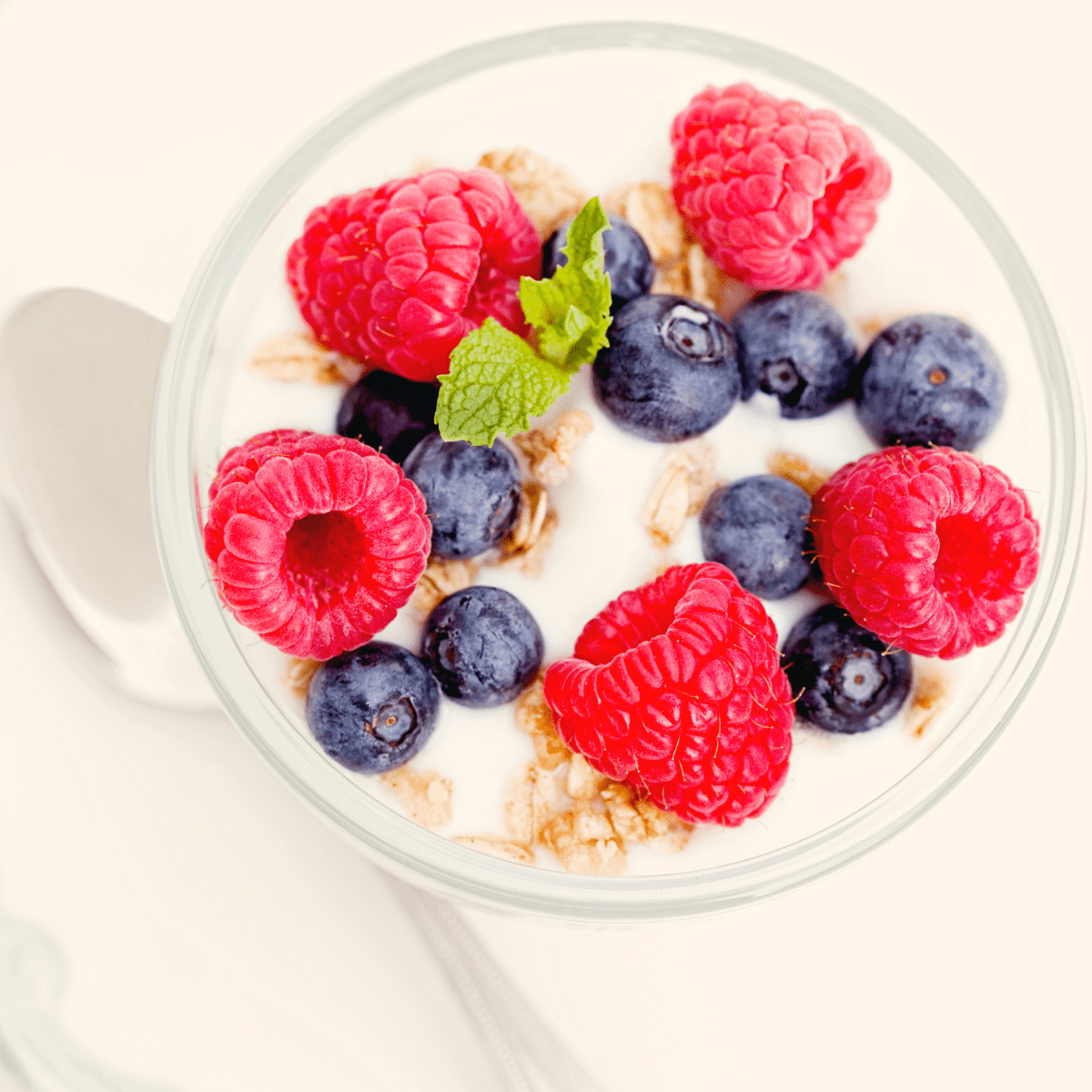 Glass bowl with white yogurt topped with granola, blueberries, raspberries and mint