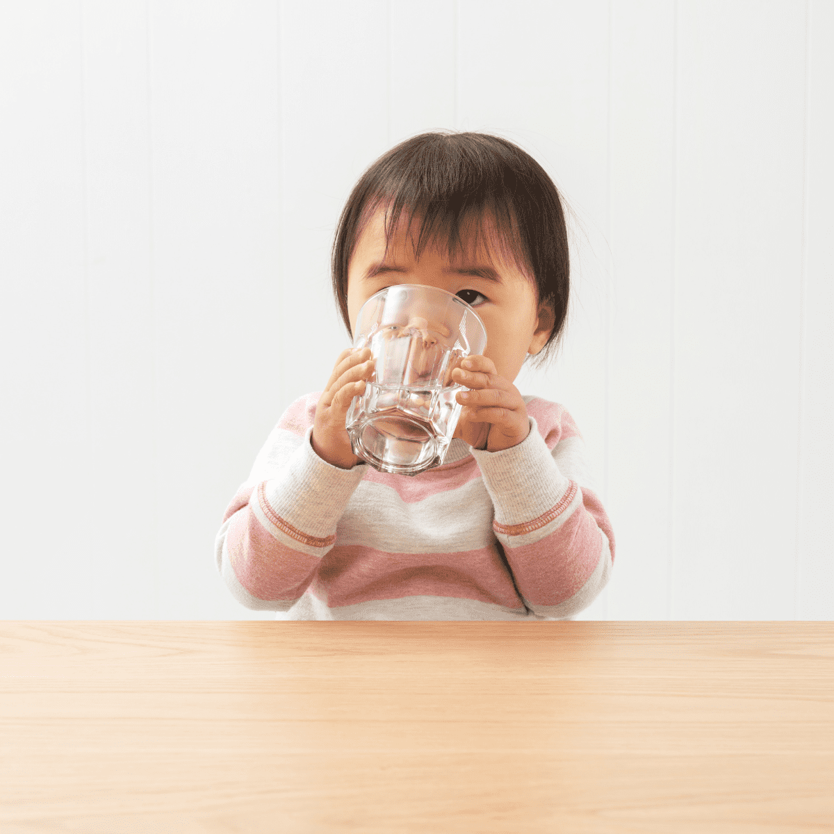 Young toddler drinking a glass of water with two hands. 