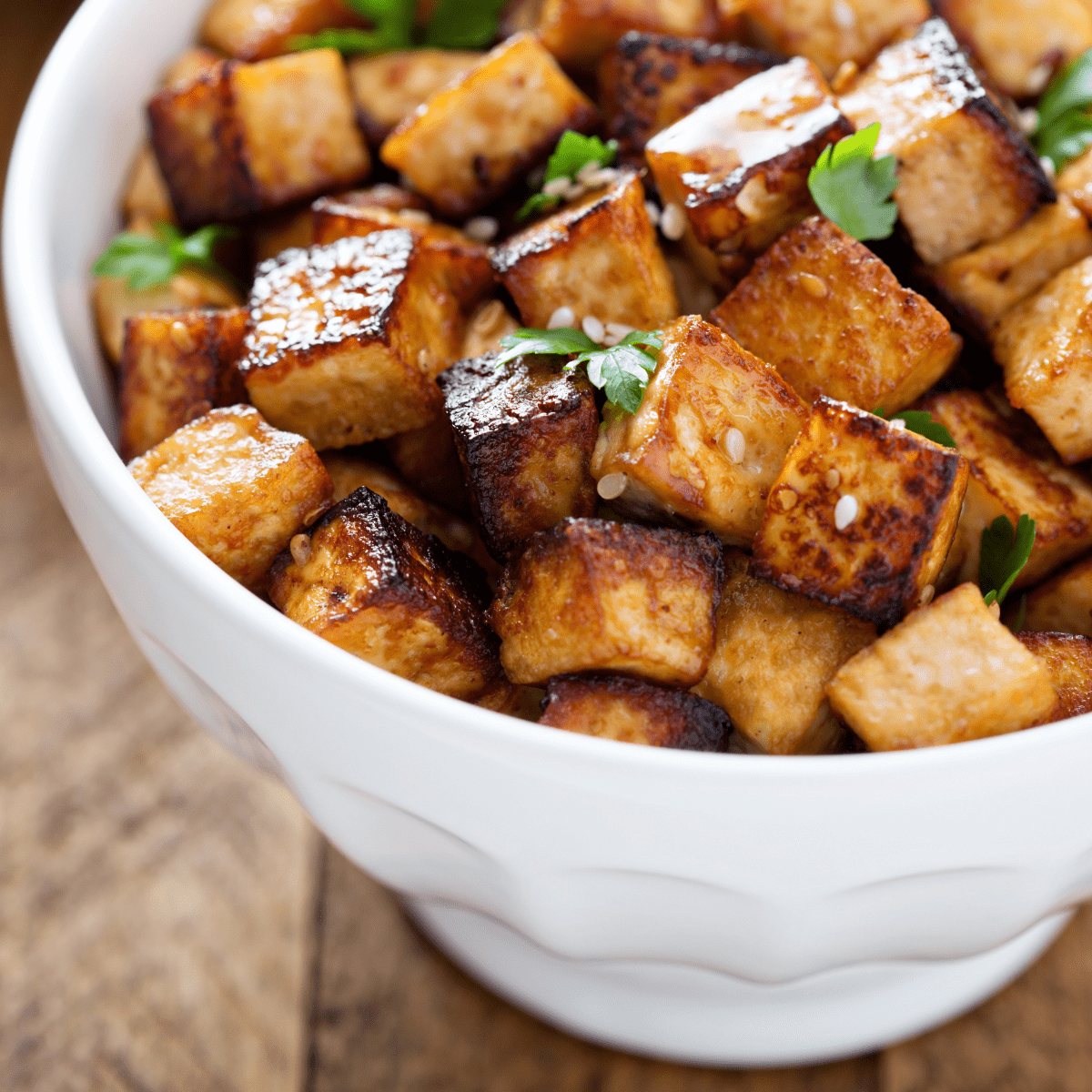 White bowl of cooked tofu with sesame seeds and parsley sprinkled on top. 