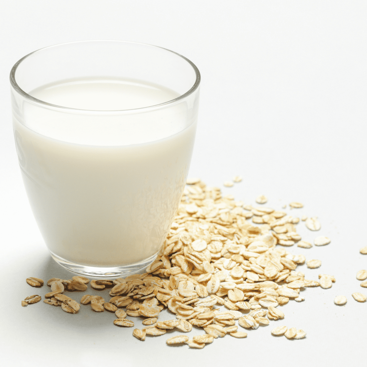 Glass of milk with oats surrounding it on a white tabletop. 