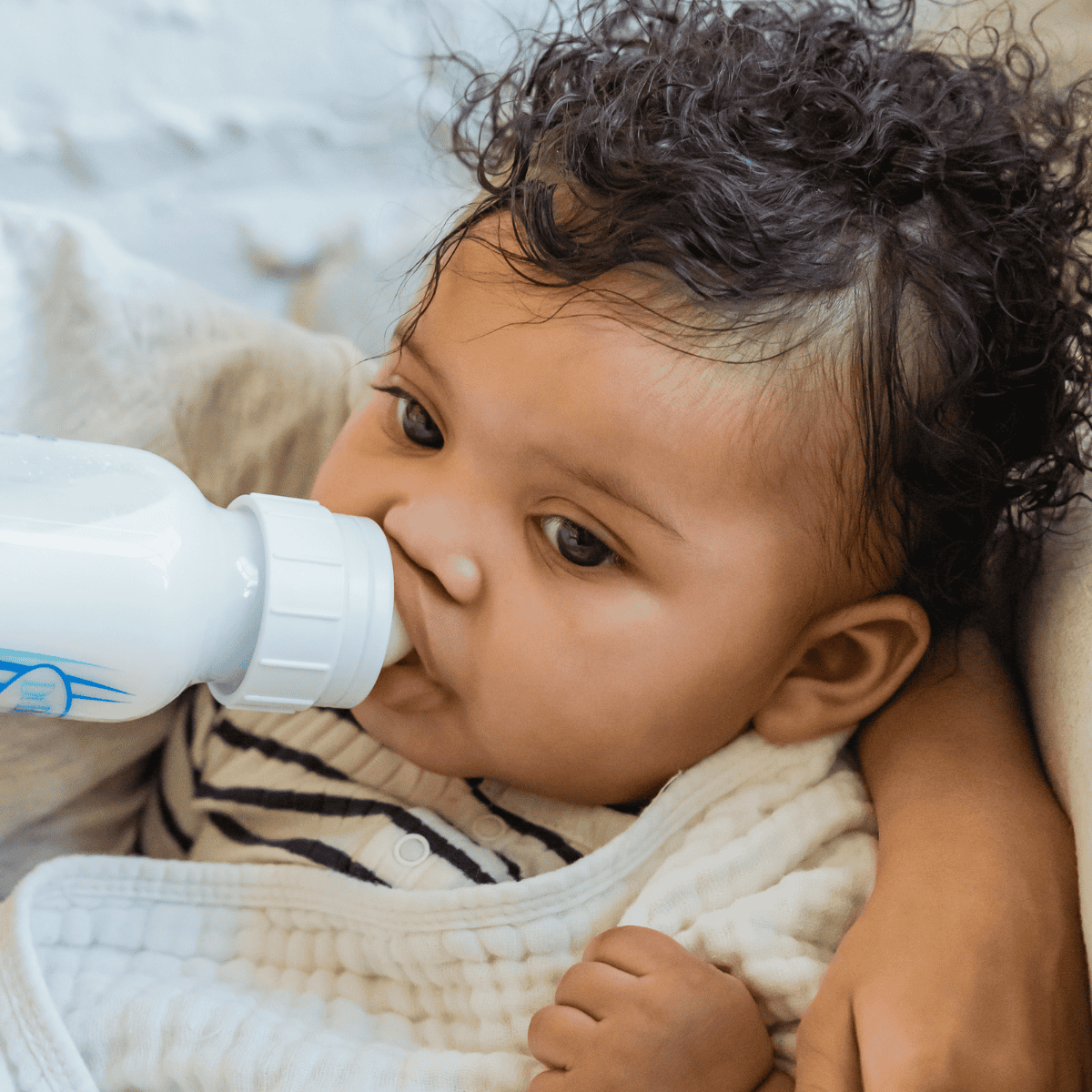 Baby wrapped in a white blanket drinking milk from a bottle.