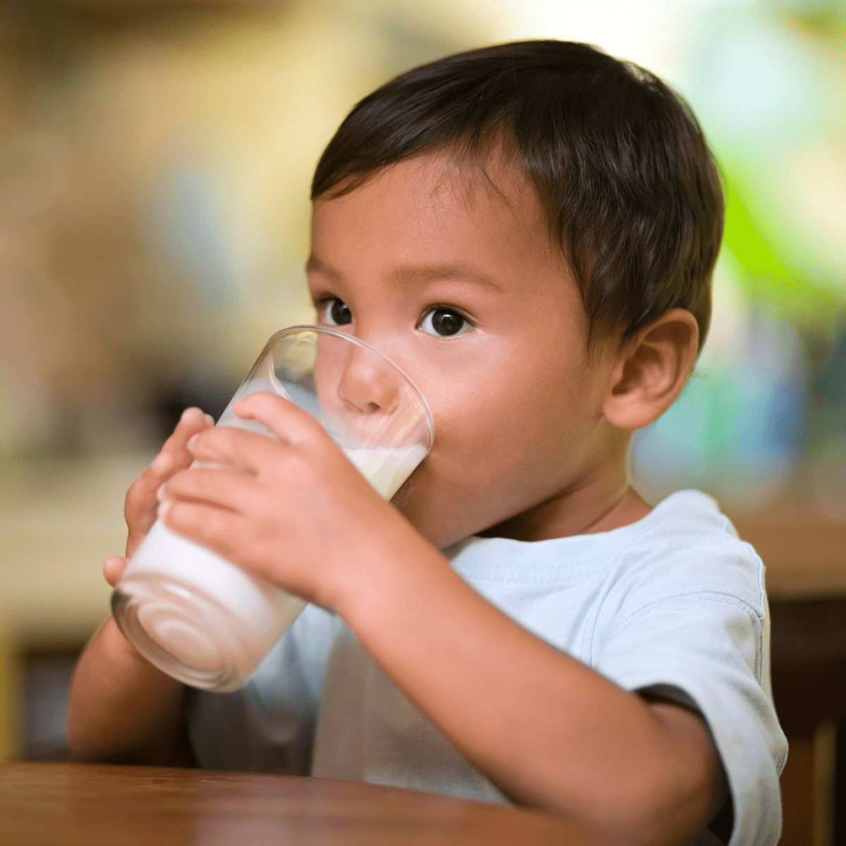 Boy with brown hair and brown eyes and white t-shirt drinking a glass of milk