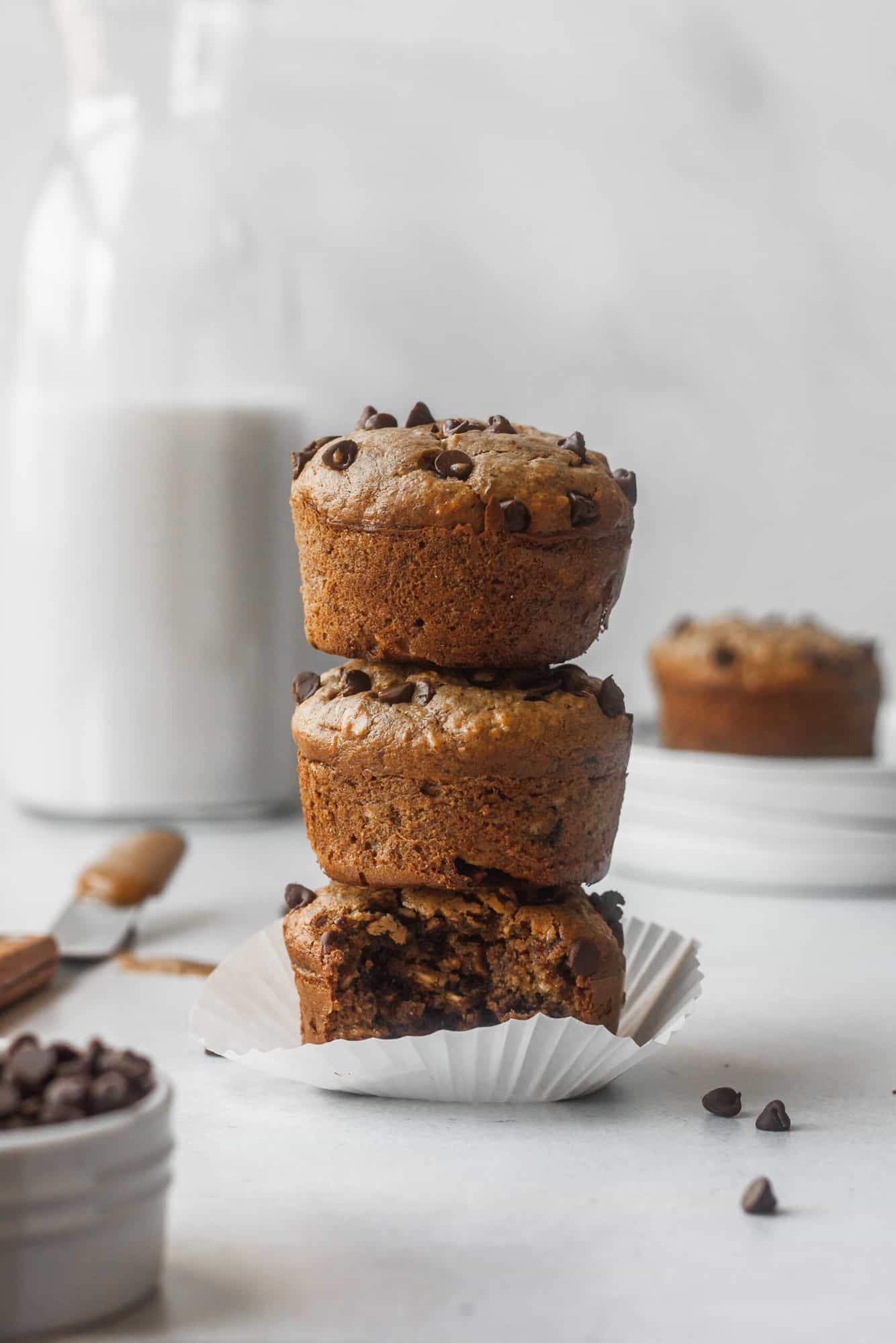 three banana chocolate chip muffins stacked with muffin and milk in the background