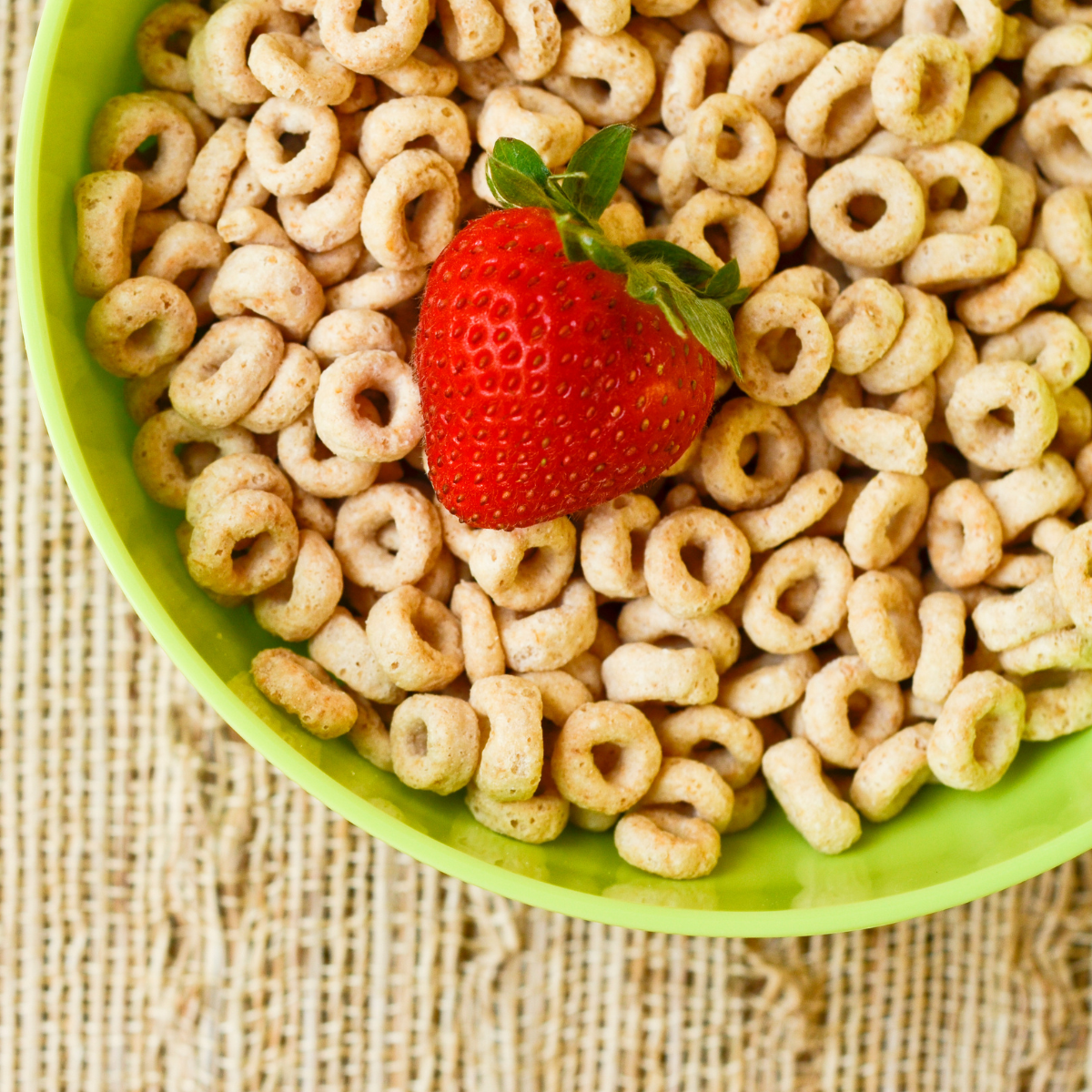 Green bowl of cheerios with a strawberry on top