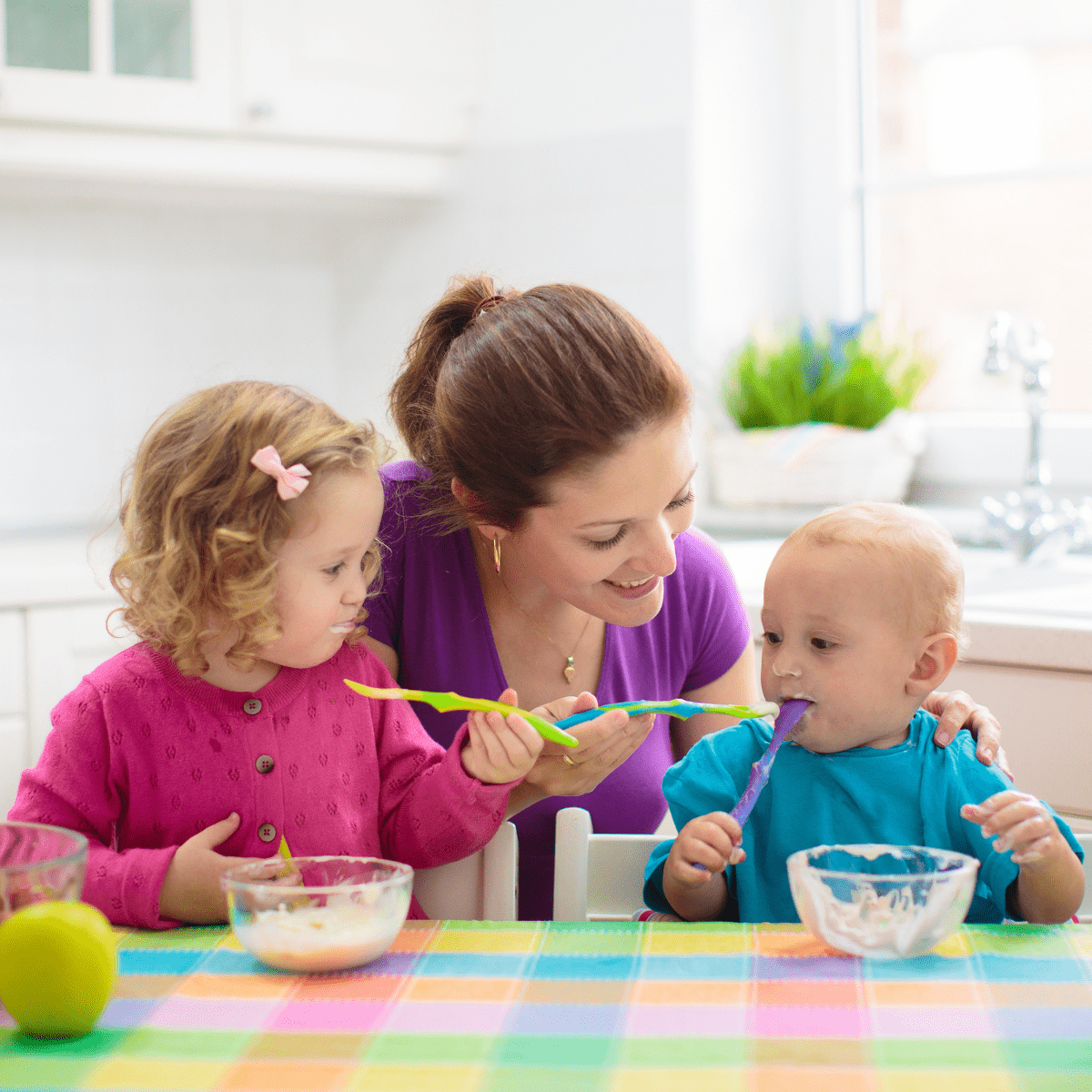 Mom at table with two children eating with plastic spoons from glass bowls.