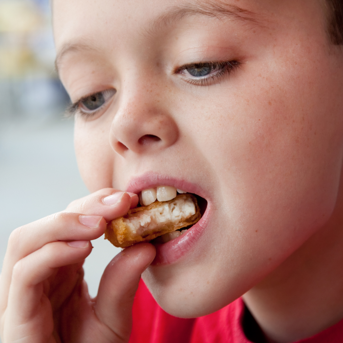 Close up of boy holding chicken nugget with hand and taking a bite.