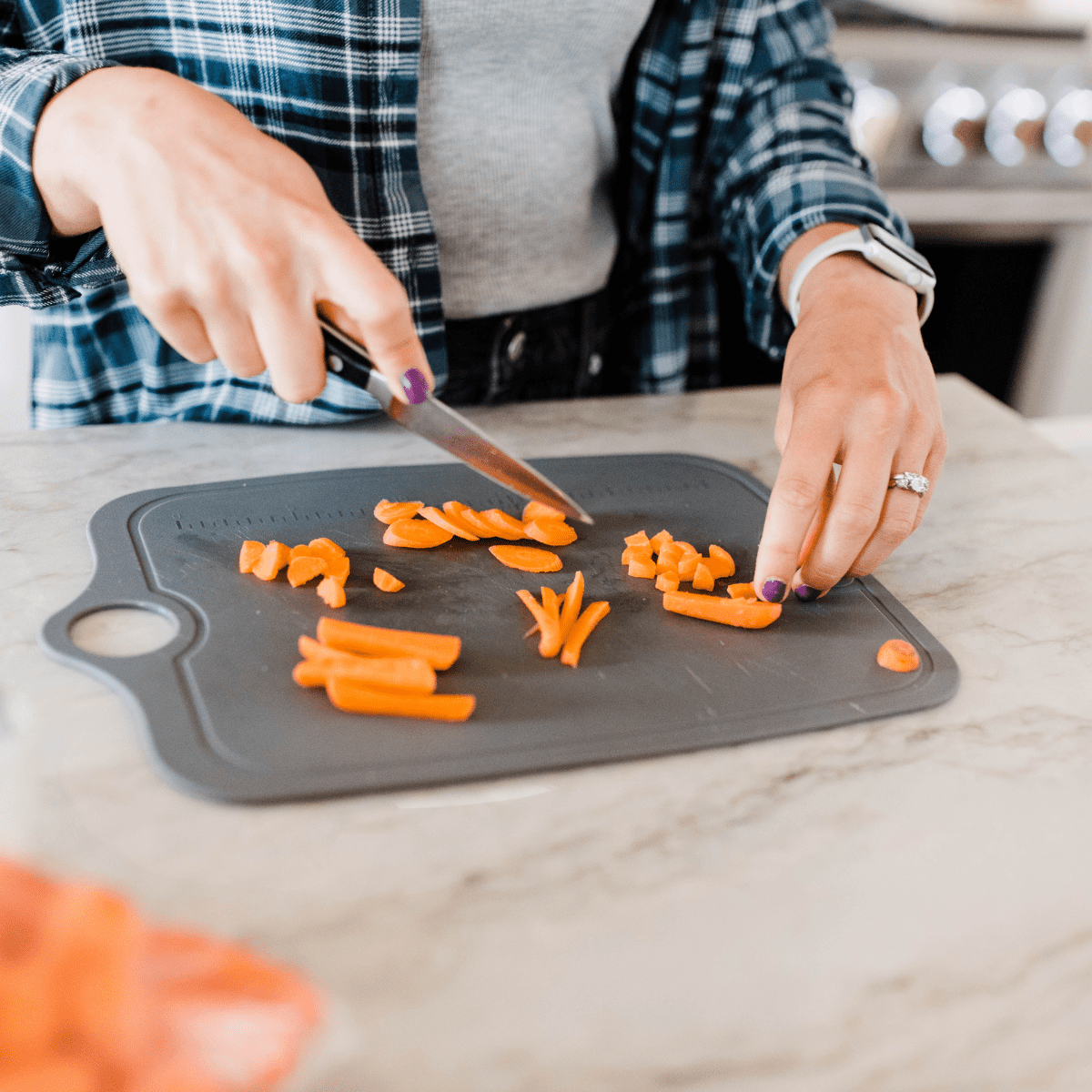 Hands with knife cutting baby carrots into different shapes and sizes on gray cutting board.