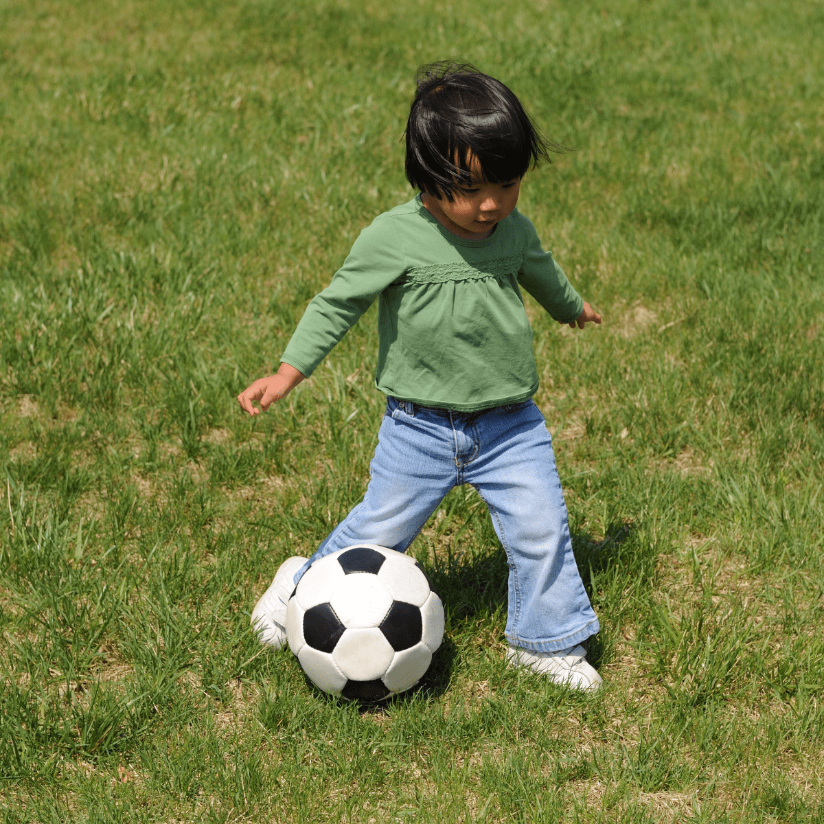 Toddler playing soccer on green grass