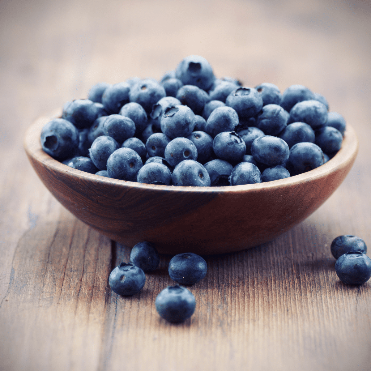 Wooden bowl full of ripe blueberries on a wooden table