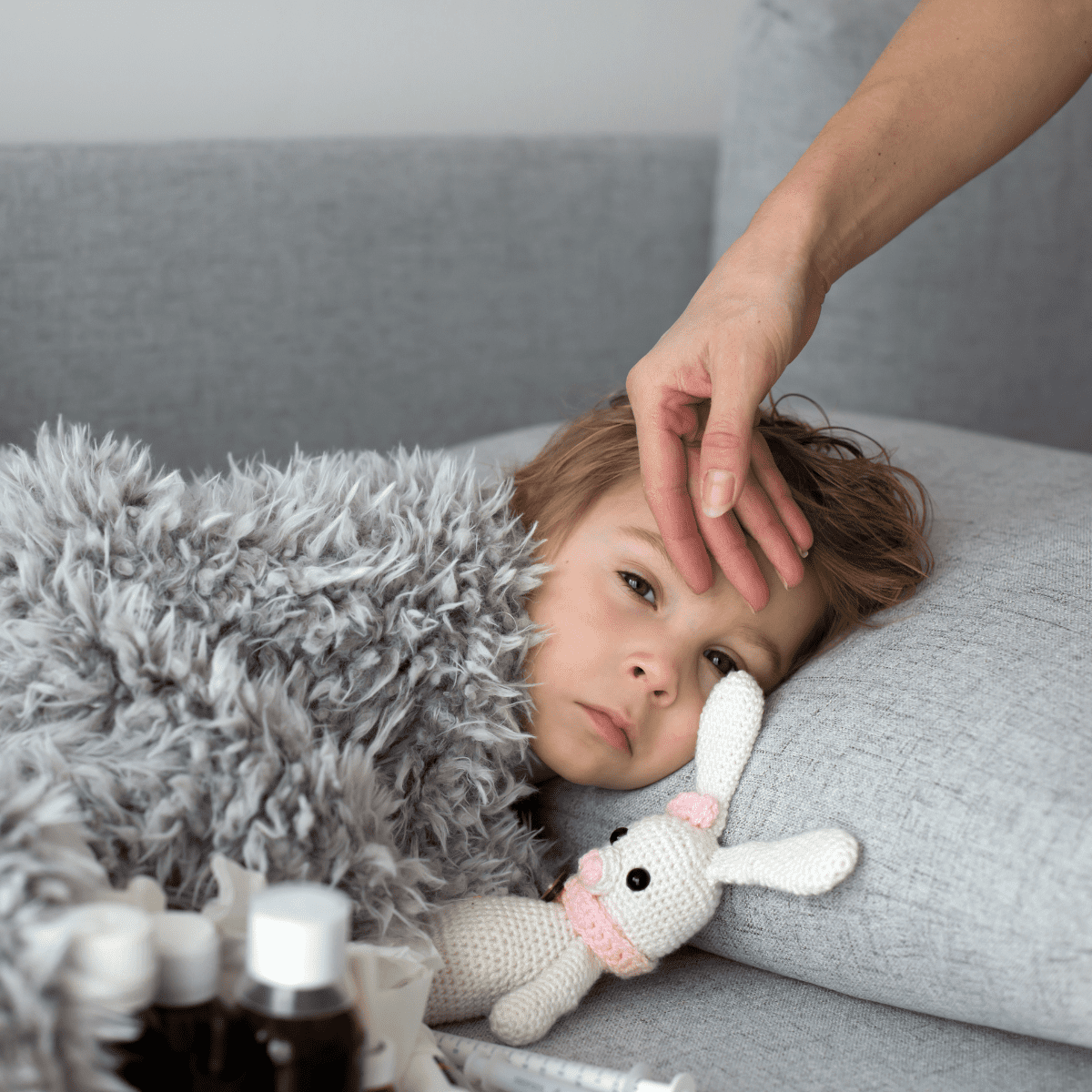 Sick child laying on couch with grey blanket, pillow and bunny stuffed animal