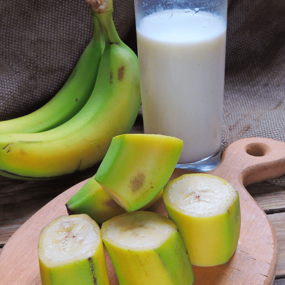 Glass of milk next to whole and sliced green bananas