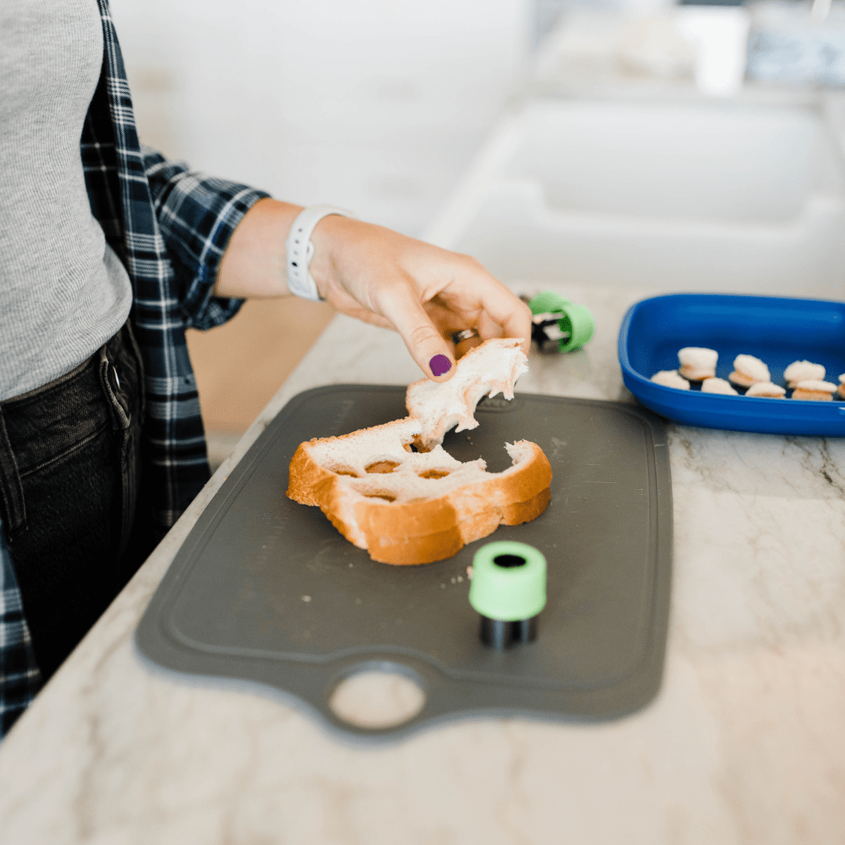 Hands cutting shapes out of a nut butter and jelly sandwhich