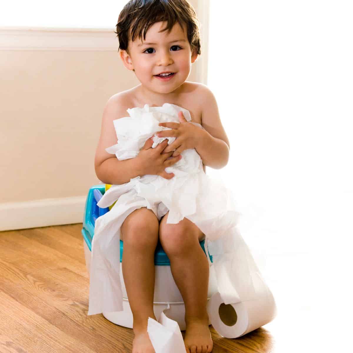 Little boy sitting on training toilet with unraveled toilet paper