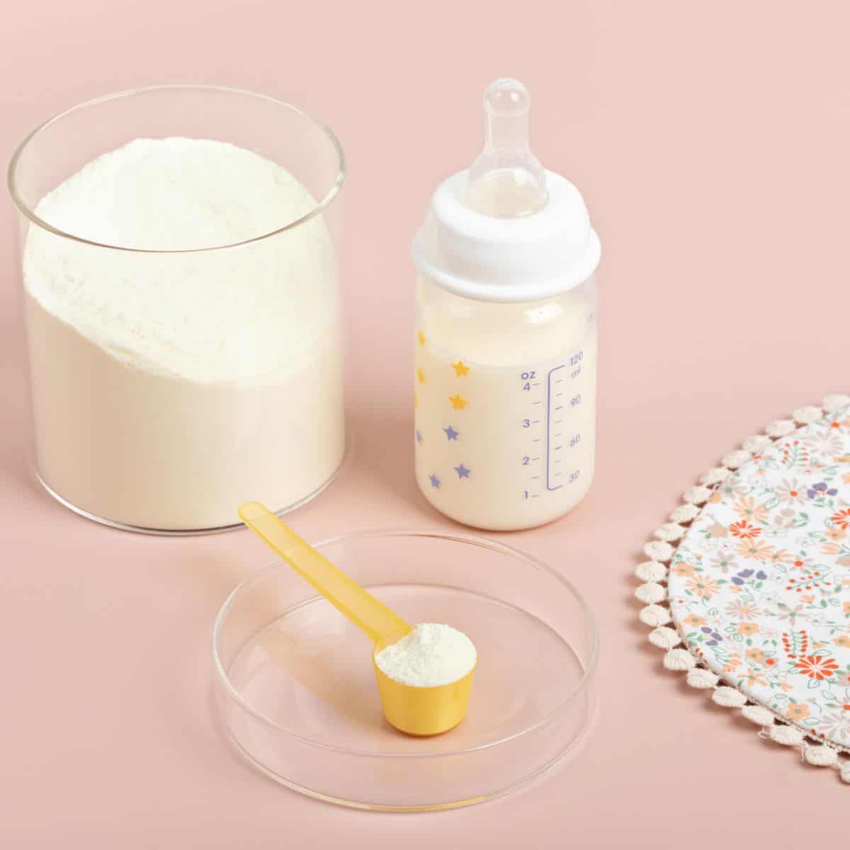 Baby formula in glass canister next to scoop and baby bottle