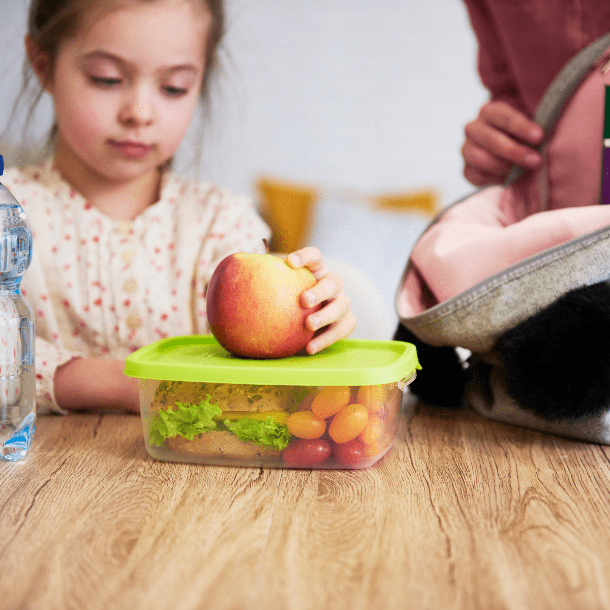 Child helping parent put lunch, snack and drink into backpack