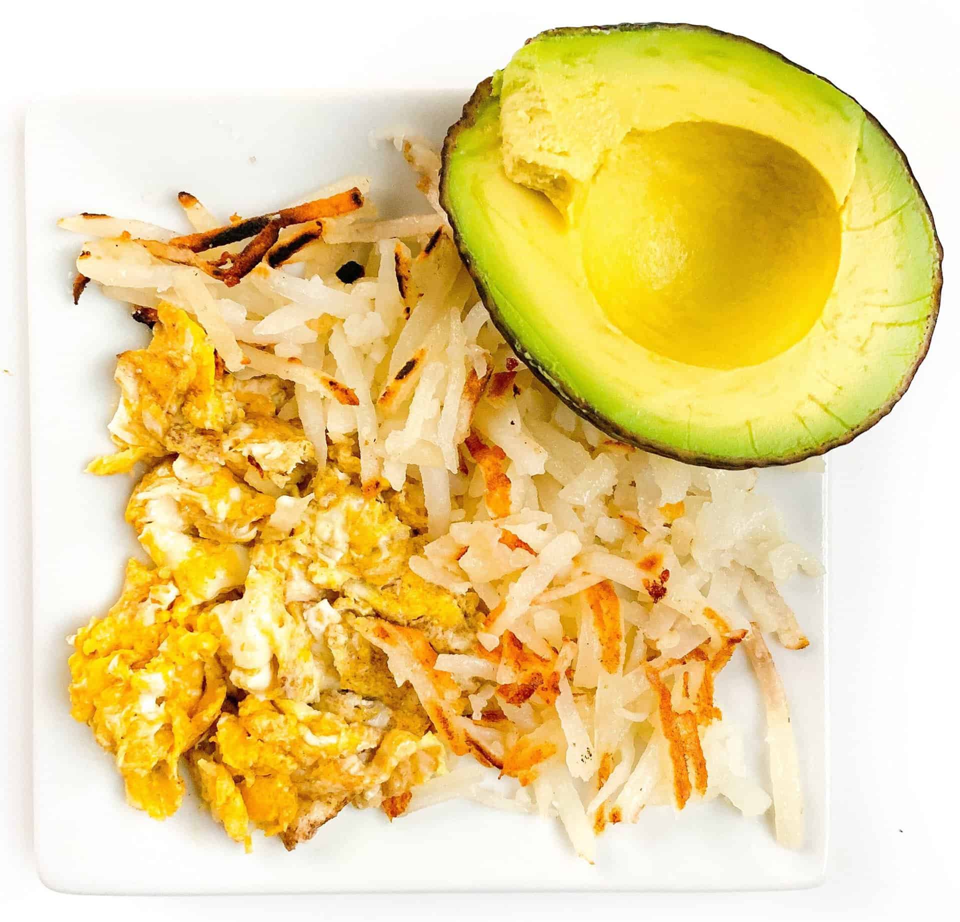 scrambled eggs, hash brown potatoes, and avocado on a white plate for a one year old breakfast