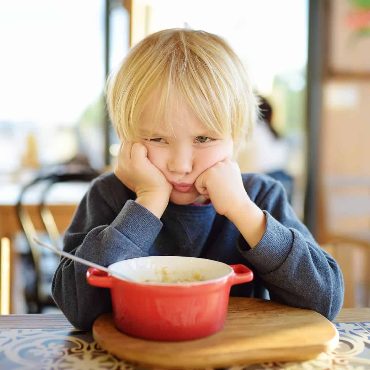 Little boy with head in hands looking unhappy, not eating from the food bowl on the table