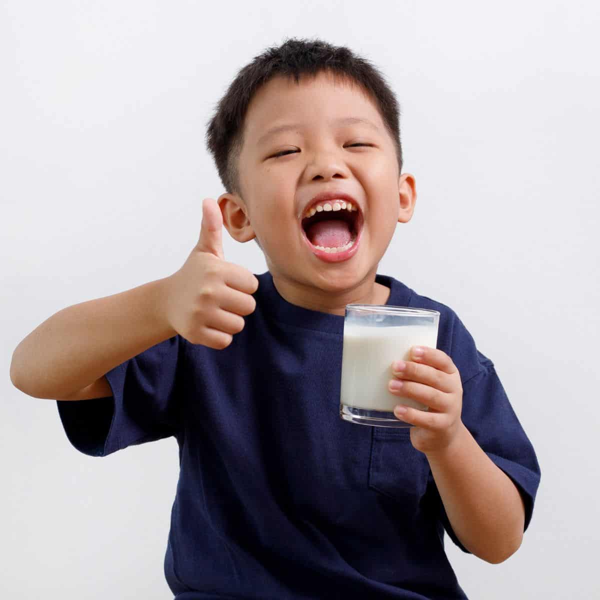 Toddler boy holding glass of milk in one hand while giving a thumbs-up with the other hand