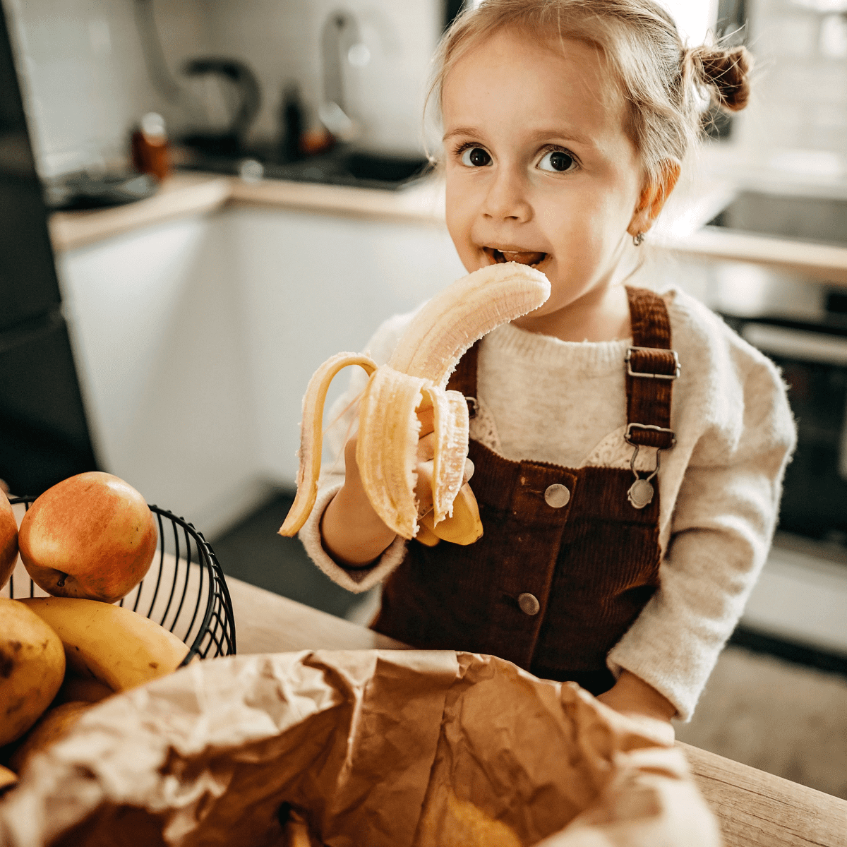 Toddler girl eating banana in kitchen