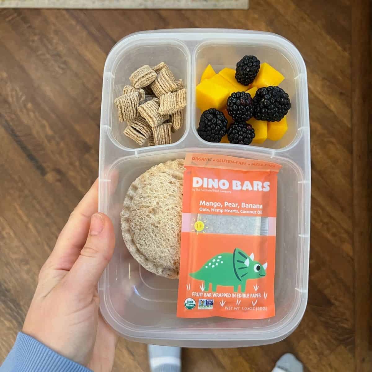 Uncrustable, berries, mango, cereal and Dino Bar in a packed lunch container