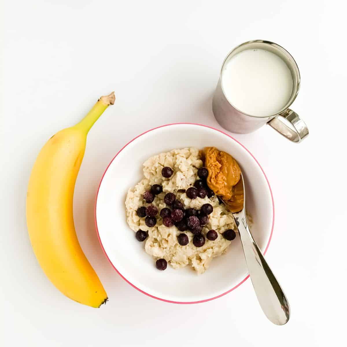 Cup of milk, unpeeled banana, oatmeal in bowl with blueberries and nut butter