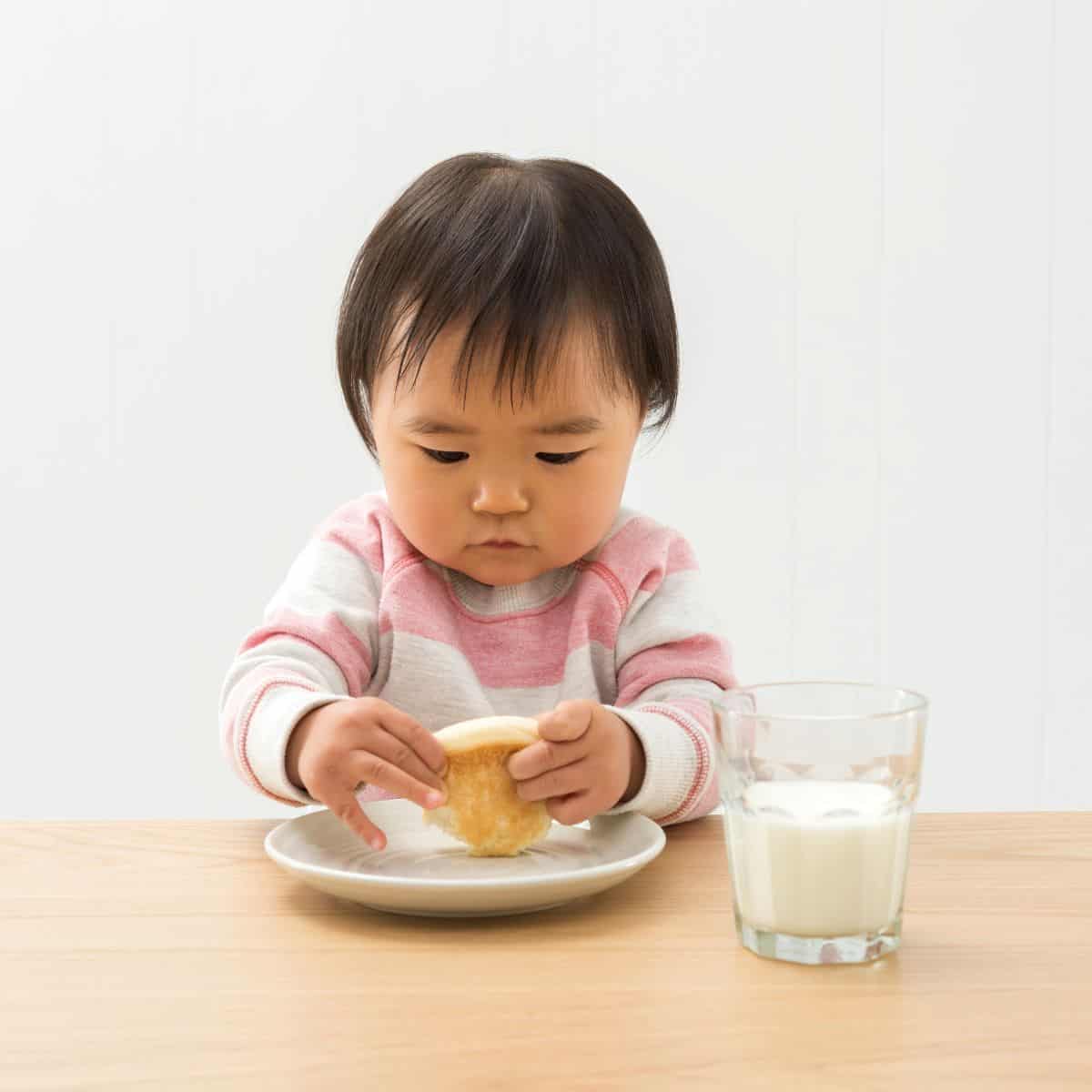 Toddler girl sitting at table eating pancakes with a glass of milk