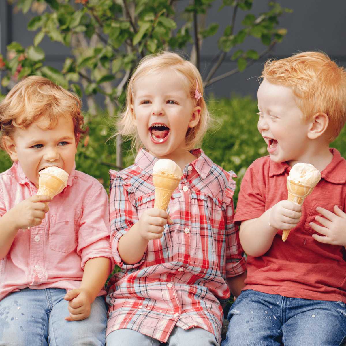 three kids sitting and eating vanilla ice cream cones outslide