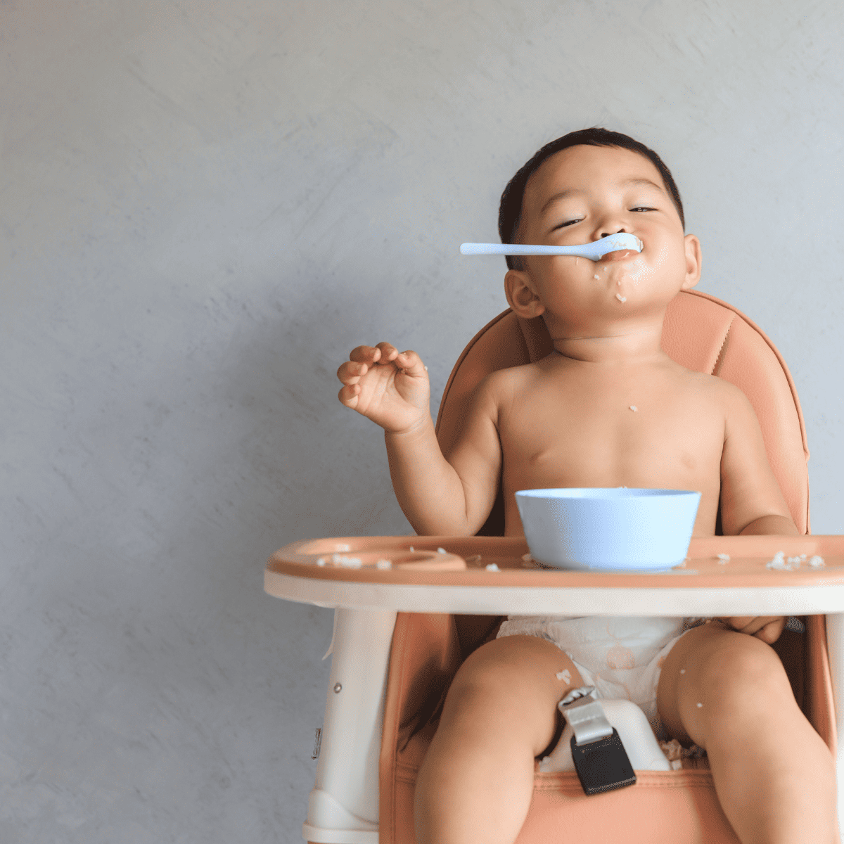 baby eating with spoon in a highchair