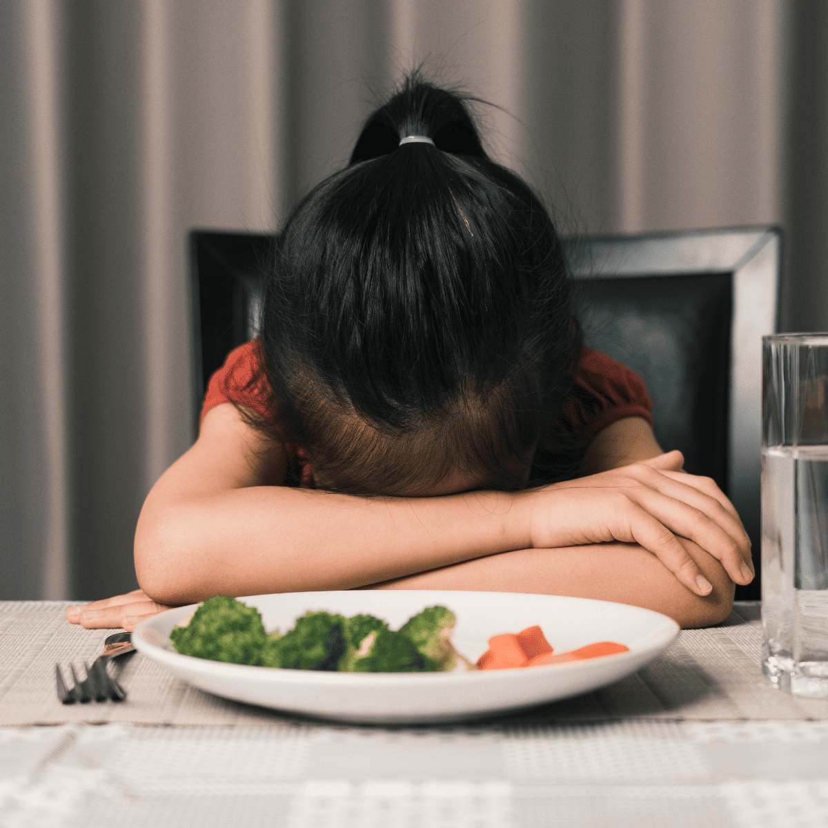 kid with head down not eating food on plate