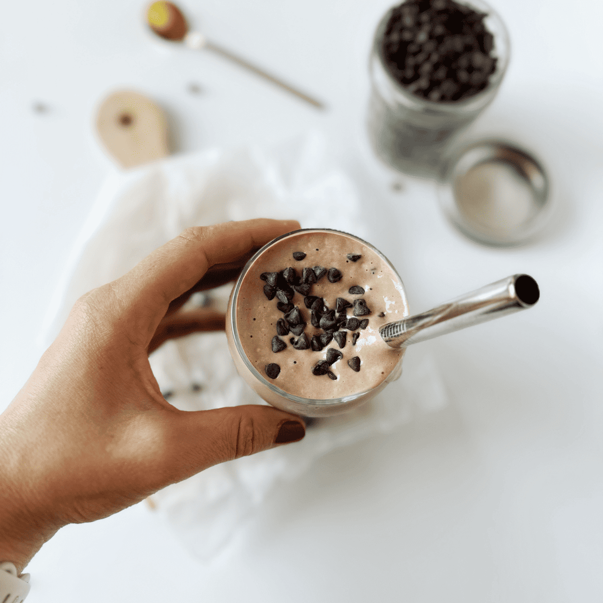 chocolate zucchini smoothie in a glass with a metal straw and chocolate chips 