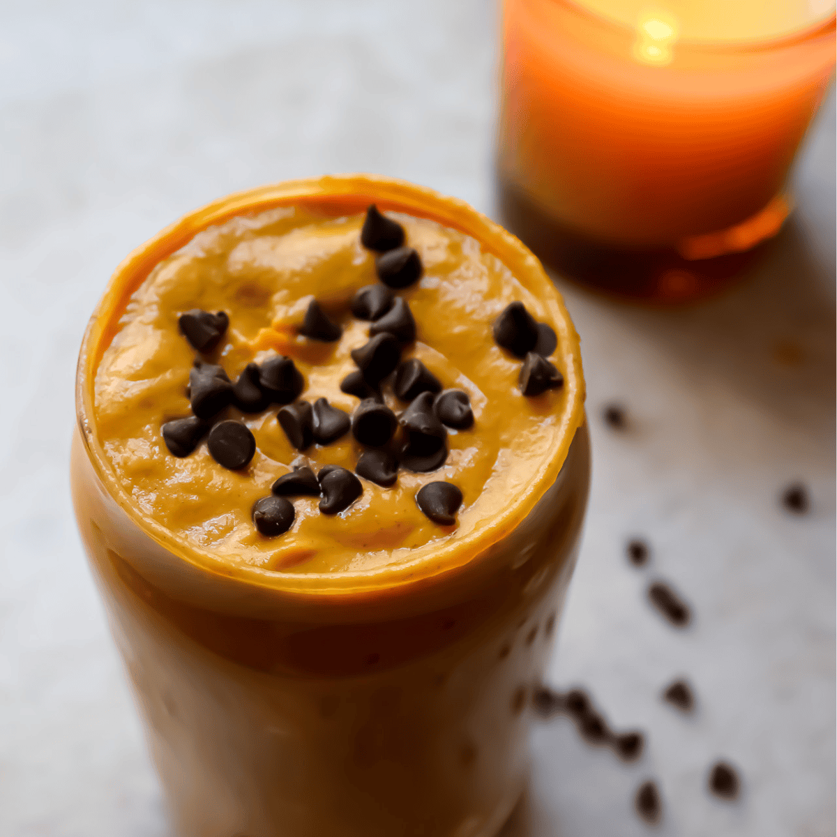 close up of pumpkin pie smoothie with candle in the background